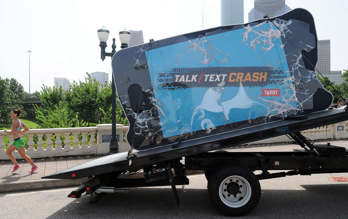 A jogger runs past an oversized cell phone on the Sabine Street bridge. The phone is part of the Talk,Text, Crash campaign that is designed to call attention to the epidemic of driver distractions in Texas.