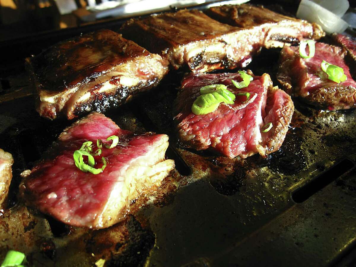 Three-bone beef short ribs cooking on the tabletop grill at Hon Machi Japanese & Korean BBQ.