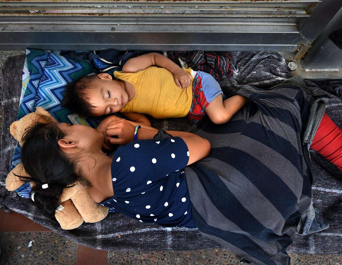 July 2, 2018 - Brownsville, Texas - Asylum seekers sleep on B/M Gateway bridge waiting to cross into U.S. from Mexico side. Ingrid Perdomo, 18 and her 1-year-old son Jose Luis take a nap in blistering heat. She came with her companion Luis Miguel, 32 from Honduras where they made the difficult 3 month journey. He said he fled in fear and cries a lot with anxiety about losing his past. His ex-wife started dating a gang member and the gang torched his home killing his 2 children inside. He fled to mountains seeking safety where he met Ingrid and they had another child. When they first arrived they said they were told by border guards they would not get in until their child was an adult, possibly as a deterrent then went to stay with a cousin in Mexico for a few days but had kidnap threats and returned to bridge July 1. They were eventually allowed in late on July 2 to be processed for credible fear. If not for a small humanitarian group Asociacion Civil Ayudandoles a Triunfar a.c. run by Glady Canas from Mexico they would have not had blankets to sleep on, food, water, etc. Carol Guzy/for San Antonio Express-News