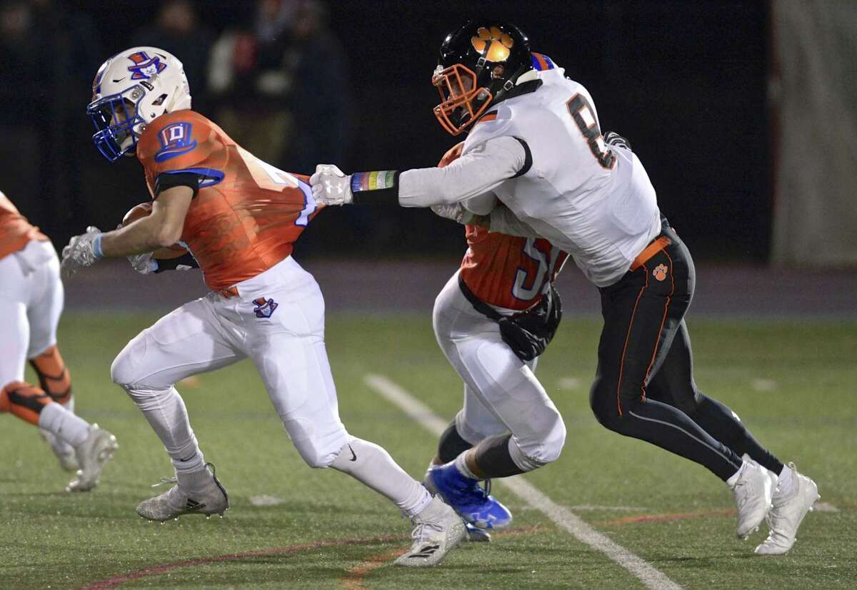 Ridgefield’s Jackson Mitchell (8) fights off a block by Bethel’s Raymond Pinto (5) to grab Danbury running back Jack Pompea (7) behind the line.