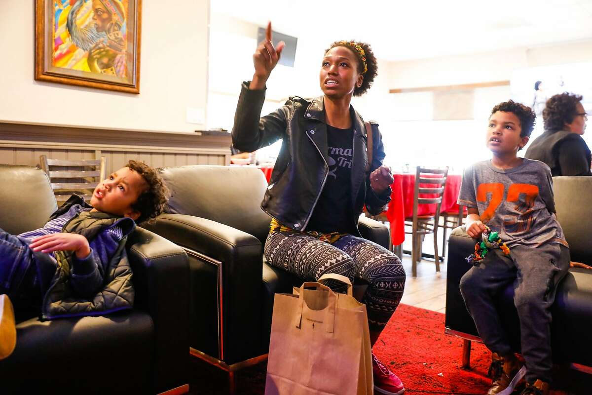 Alicia Langlais (center) watches television with her kids Solomon, 6 (right) and Malakai, 4 after grabbing food to-go at Kendejah, the Bay Area's only Liberian restaurant in San Leandro, California, on Sunday, Nov. 25, 2018.