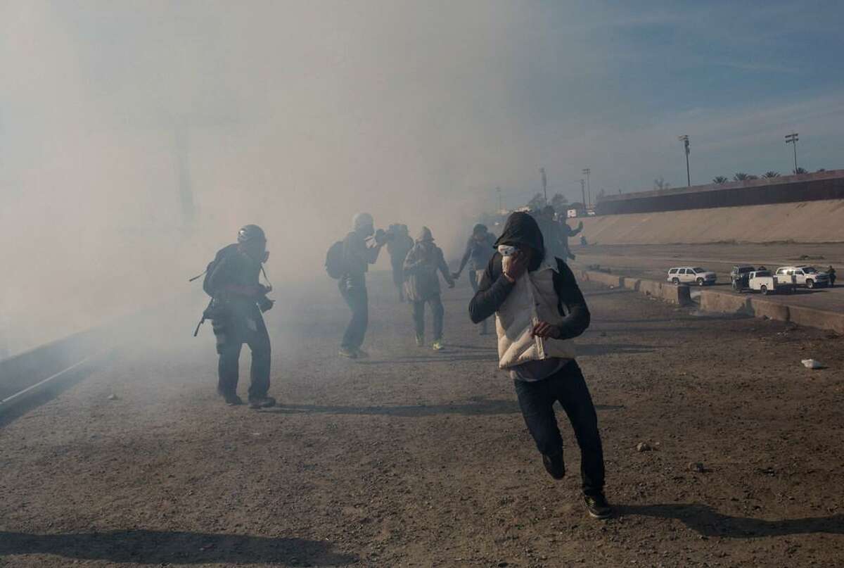 Migrants run from tear gas launched by U.S. agents, amid photojournalists covering the Mexico-U.S. border, after a group of migrants got past Mexican police at the Chaparral crossing in Tijuana, Mexico, Sunday, Nov. 25, 2018. The mayor of Tijuana has declared a humanitarian crisis in his border city and says that he has asked the United Nations for aid to deal with the approximately 5,000 Central American migrants who have arrived in the city. (AP Photo/Rodrigo Abd)