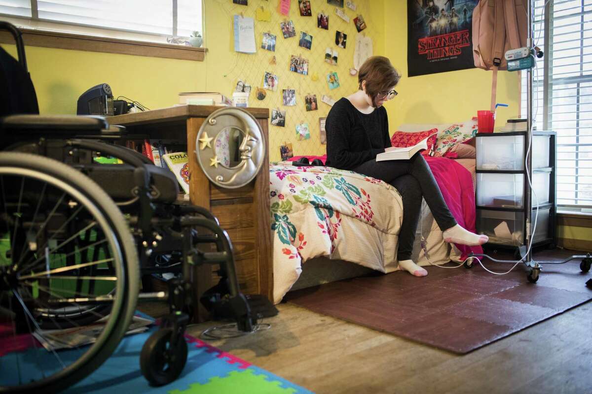 Katie Hebert, 13, reads a book in her bedroom next to her wheel chair and feeding tube, Wednesday, Nov. 28, 2018 in Pasadena. Hebert has a disorder on which her body has difficulties metabolizing food and oxygen to generate energy.