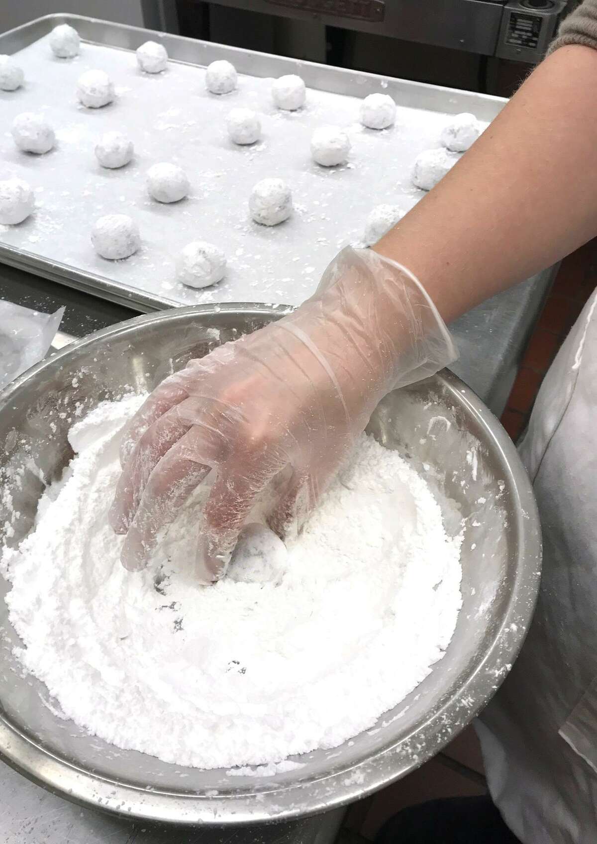 A worker at Crumb Together Bakery in Norwalk rolls a chocolate crinkle cookie ball in powdered sugar before baking.