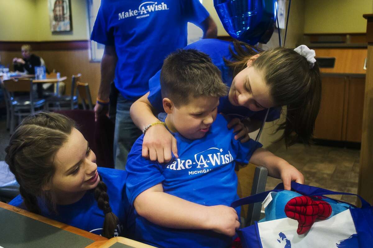 Cutler Doud, 7, center, opens a gift from the staff at Culver's alongside two of his sisters, Tirzah, 16, left, and Thea, 14, right, during a going-away party Sunday, Dec. 2, 2018 for the Doud family's upcoming Disney cruise arranged by Make-A-Wish. (Katy Kildee/kkildee@mdn.net)