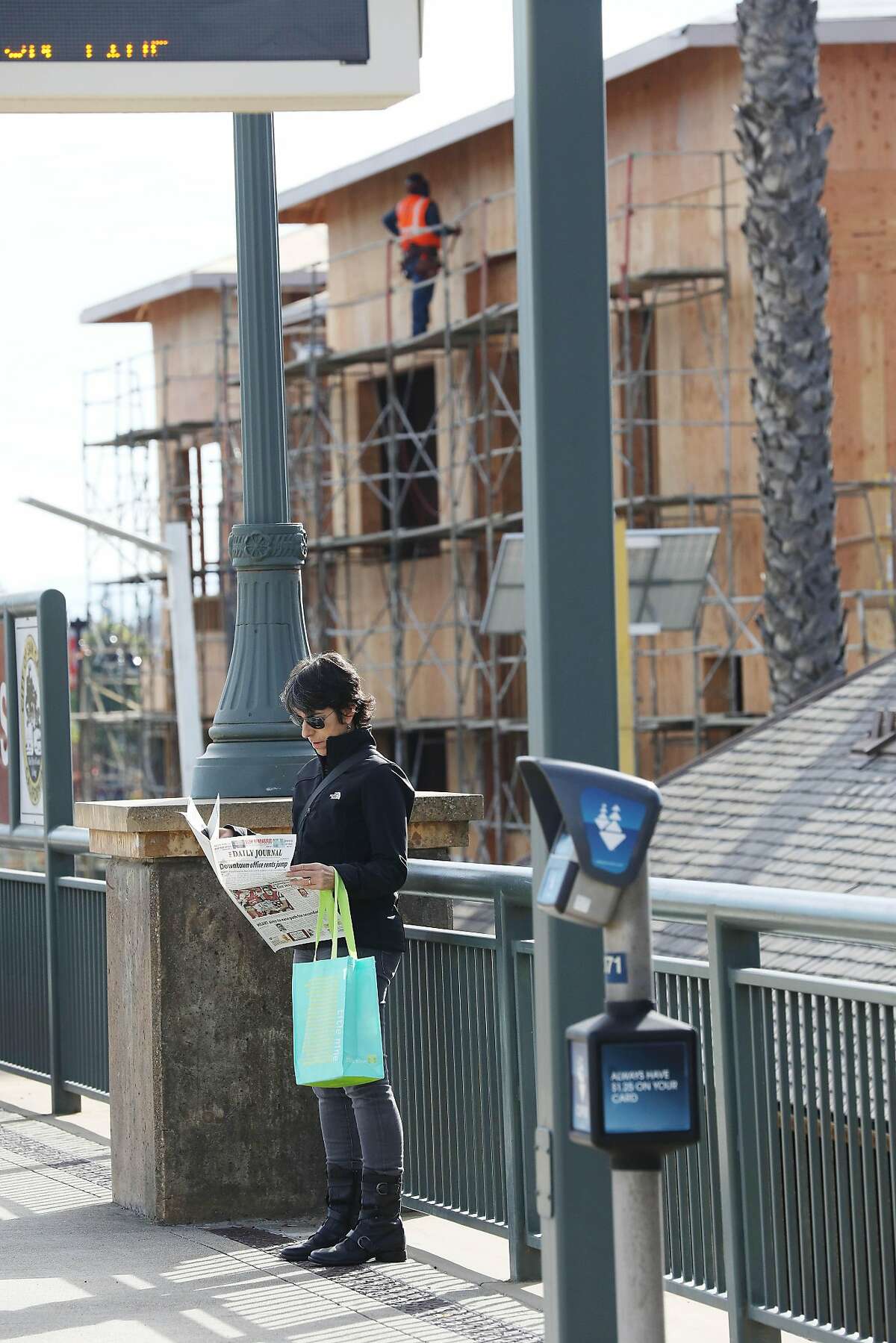 Robin Weiss of San Carlos waits for a train at the San Carlos Caltrain station while behind her new construction on El Camino Real can be seen on Monday, December 3, 2018 in San Carlos, Calif.