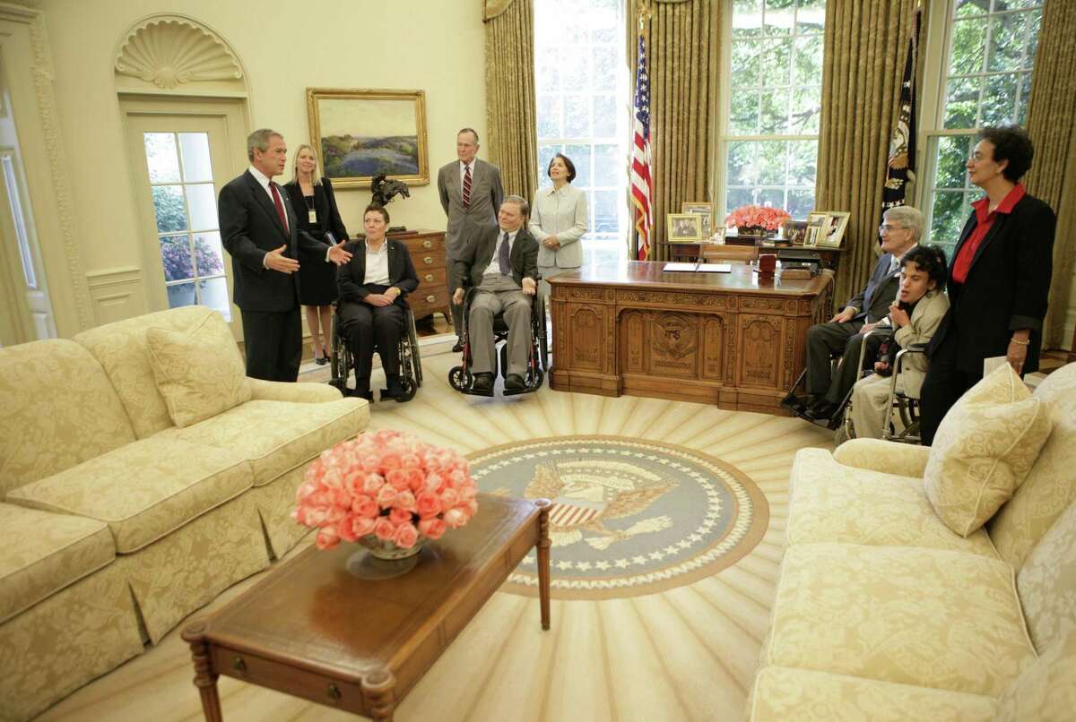 In this July 2005 White House, President George W. Bush gives a tour of the Oval Office after the signing of the Presidential Proclamation to Commemorate the 15th anniversary of the Americans with Disabilities Act. Meeting participants from left: President Bush; Susan Buckland, associate director of the Domestic Policy Council; Jan Tuck, chair, Architectural and Transportation Barriers Compliance Access Board; former President George H.W. Bush; Dr. Lex Frieden, chair, National Council on Disability; Madeleine Will, chair, President’s Committee for People with Intellectual Disabilities; Mike Deland, former director of White House Council on Environmental Quality under President George H.W. Bush; and Lucy Aponte and Berthy De La Rosa-Aponte, chair, Ticket to Work and Work Incentives Advisory Panel.