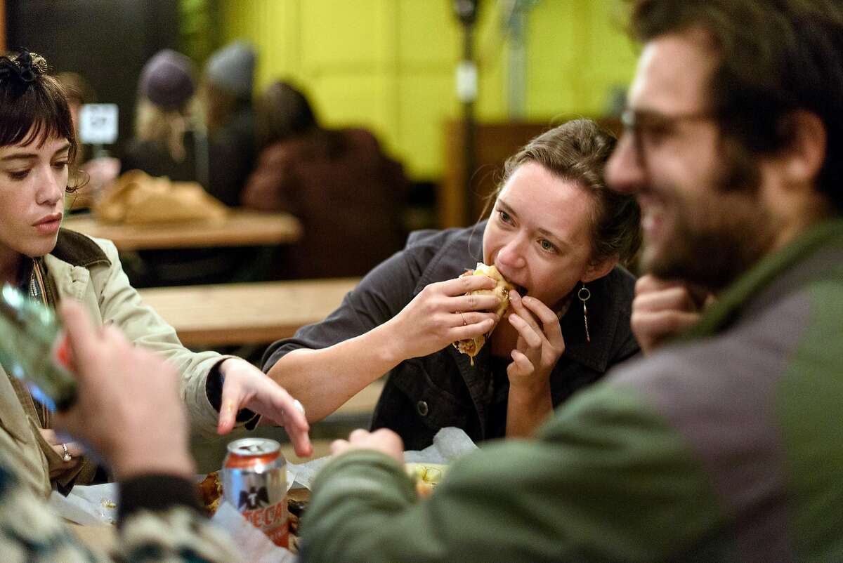 Cayley Eller bites into a taco as she and Syd Skorich, left, and Arlo Perlstein eat at Tacos Oscar's new permanent home in Oakland, California, on Friday, November 30, 2018.