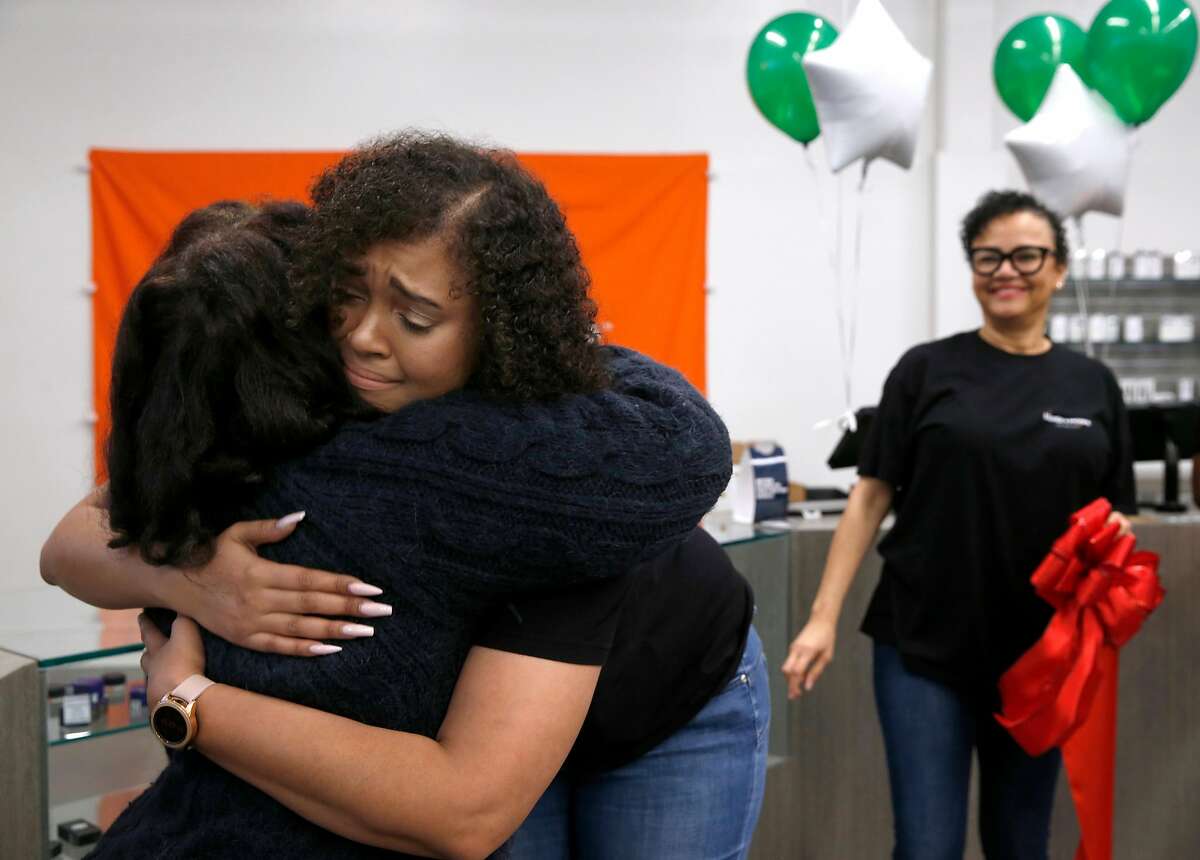 Brittany Moore hugs Desley Brooks (left) after the ribbon was cut to open the Blunts + Moore cannabis dispensary she co-owns with Alphonso Blunt in Oakland, Calif. on Thursday, Nov. 29, 2018, the first dispensary to open through the city's cannabis equity program. Watching at right is Brittany’s mother Phae Moore.