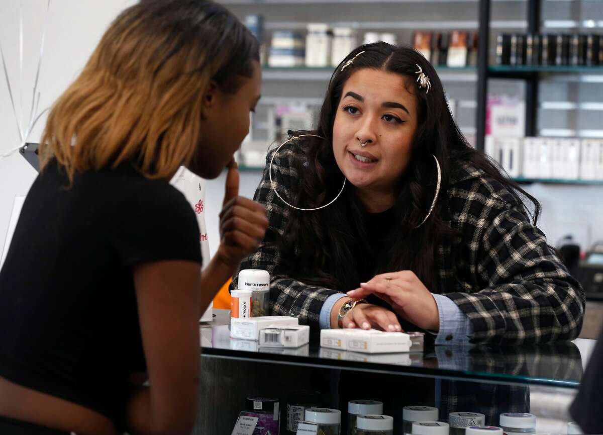 Isabella Coloma (right) helps a customer select products at the Blunts + Moore cannabis dispensary in Oakland, Calif. on Thursday, Nov. 29, 2018, the first dispensary to open through the city's cannabis equity program.