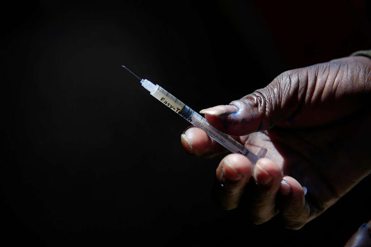 A person holds a syringe containing a hit of heroin on a Tenderloin sidewalk.