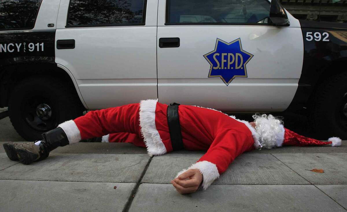A man dressed as Santa Claus lies next to a San Francisco Police car after Santa Con patrons were pushed out of Union Square in preparation for a possible protest during the 20th Annual Santa Con in San Francisco, Calif. Saturday, December 13, 2014.
