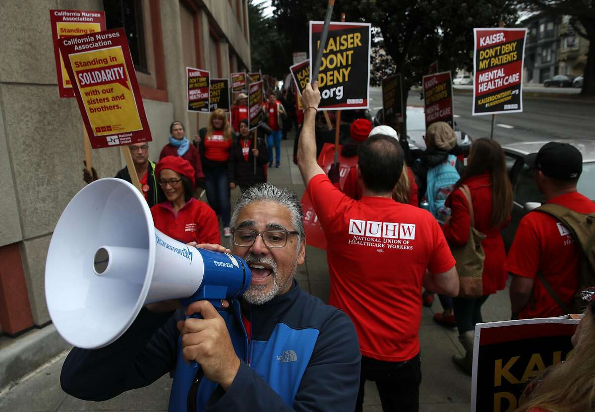 SAN FRANCISCO, CALIFORNIA - DECEMBER 10: A Kaiser Permanente mental health worker uses a bullhorn while others carry signs as they march in front of Kaiser Permanente San Francisco Medical Center on December 10, 2018 in San Francisco, California. Nearly 4,000 Kaiser Permanente mental health workers with the National Union of Healthcare Workers union kicked off a five-day strike at Kaiser facilities throughout California. The union says that they are protesting the lack of staffing that forces many patients to wait for a month or more for appointments. (Photo by Justin Sullivan/Getty Images)