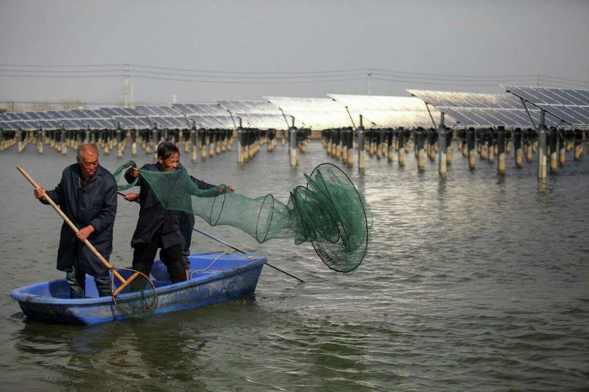 Chinese fishermen cast a net next to a photovoltaic power station built on top of fish ponds in Yangzhou in China's eastern Jiangsu province. (Photo by STR / AFP) / China OUTSTR/AFP/Getty Images