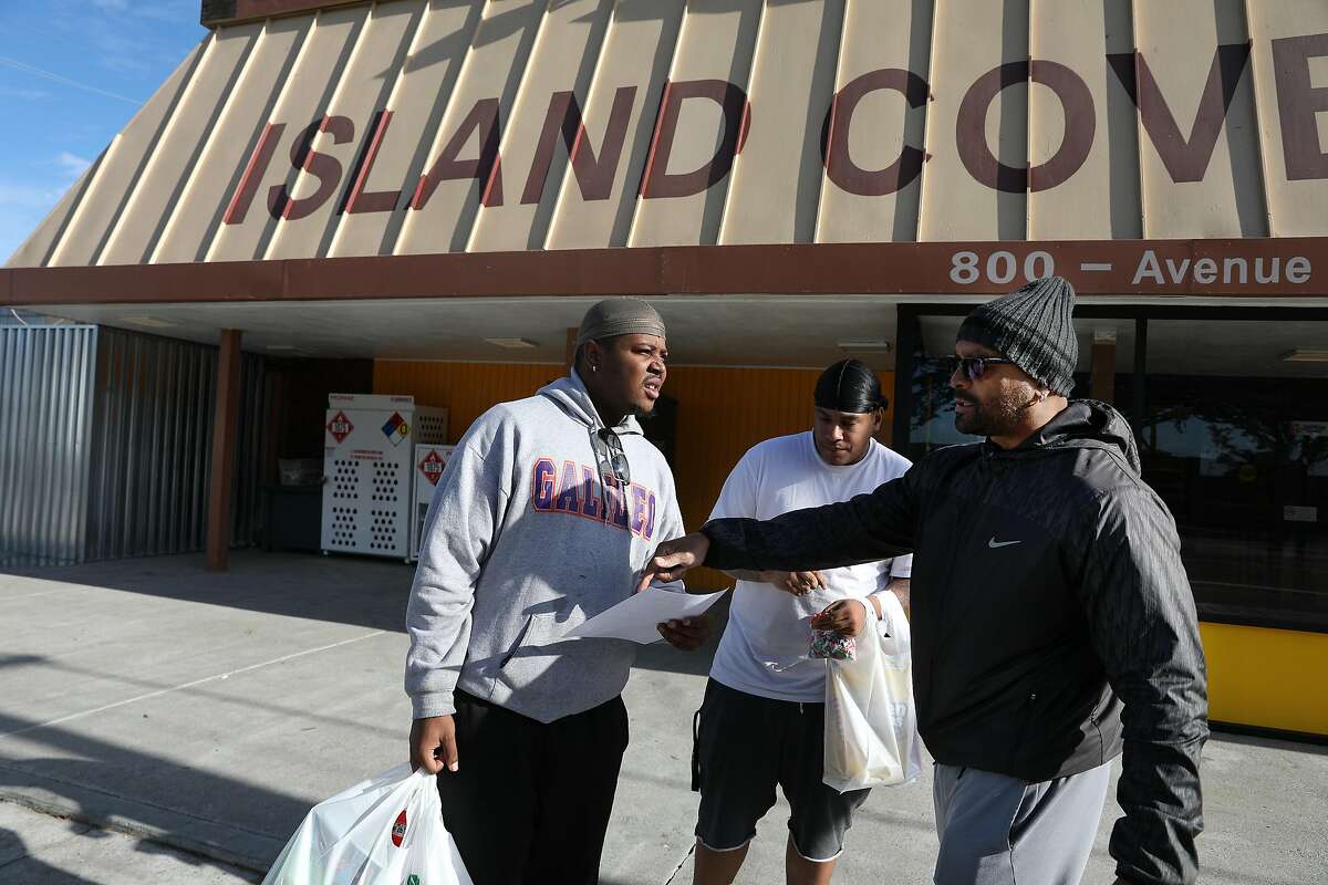 Paris Hayes (right) talks with Terrell Jeffery (left), and Terrance Oliver (partially seen center), both Treasure Island residents, in front of the Island Cove Market as he hands a flyers to encourage attendance to a City Hall meeting on Friday, Dec. 7, 2018 on Treasure Island in San Francisco. San Francisco supervisors on Tuesday delayed voting on whether to charge tolls of up to $3.50 to enter and exit Treasure Island — a plan that infuriated residents and merchants, even though transit officials said it was necessary to prevent gridlock on the Bay Bridge.