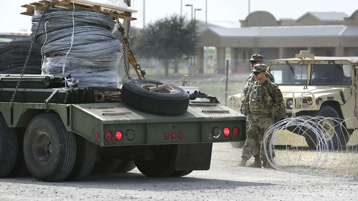Military personel hold open a razor wire gate to let in a shipment of more wire at the military camp next to the Donna-Rio Bravo International Bridge, on Tuesday, Dec. 4, 2018.