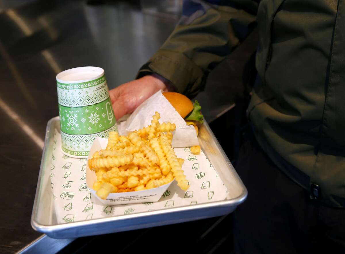 Ronald Miller carries away the first burger off the grill and the first fries out of the fryer after the first Shake Shack restaurant in Northern California opens at the Stanford Shopping Center in Palo Alto, Calif. on Saturday, Dec. 15, 2018.