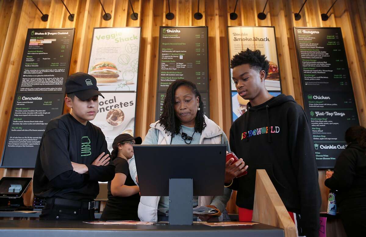 Employee Justin Ramirez (left) helps Anna Hodges and her son Tiere place their order after the first Shake Shack restaurant in Northern California opens at the Stanford Shopping Center in Palo Alto, Calif. on Saturday, Dec. 15, 2018.