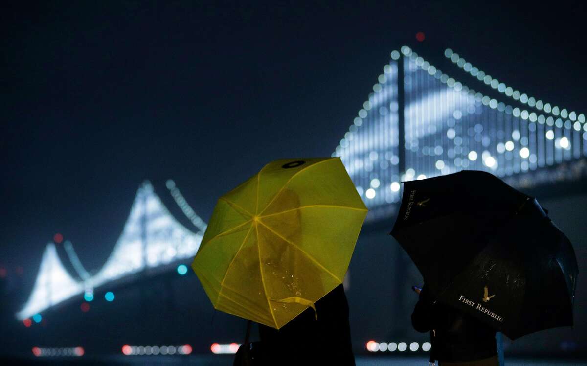Ellen Pham, left, and Michelle Sheu, right, look out over the Bay Bridge Lights as rain falls along the Embarcadero in San Francisco, Calif., on Sunday, December 16, 2018. The regions is poised to see a week of rainy weather.