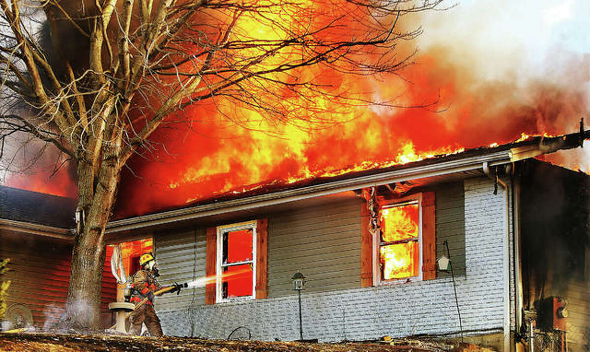 A firefighter directs a hose line through the window of a house Tuesday afternoon in the 4800 block of Rocky Branch Road in rural Dorsey as flames consume the roof and contents of the house. Smoke from the fire was visible from the east side of Alton. Firefighters from Dorsey, Fosterburg, Holiday Shores, Bunker Hill, Prairetown and Bethalto battled the fire but the house was a total loss. No injuries were reported.
