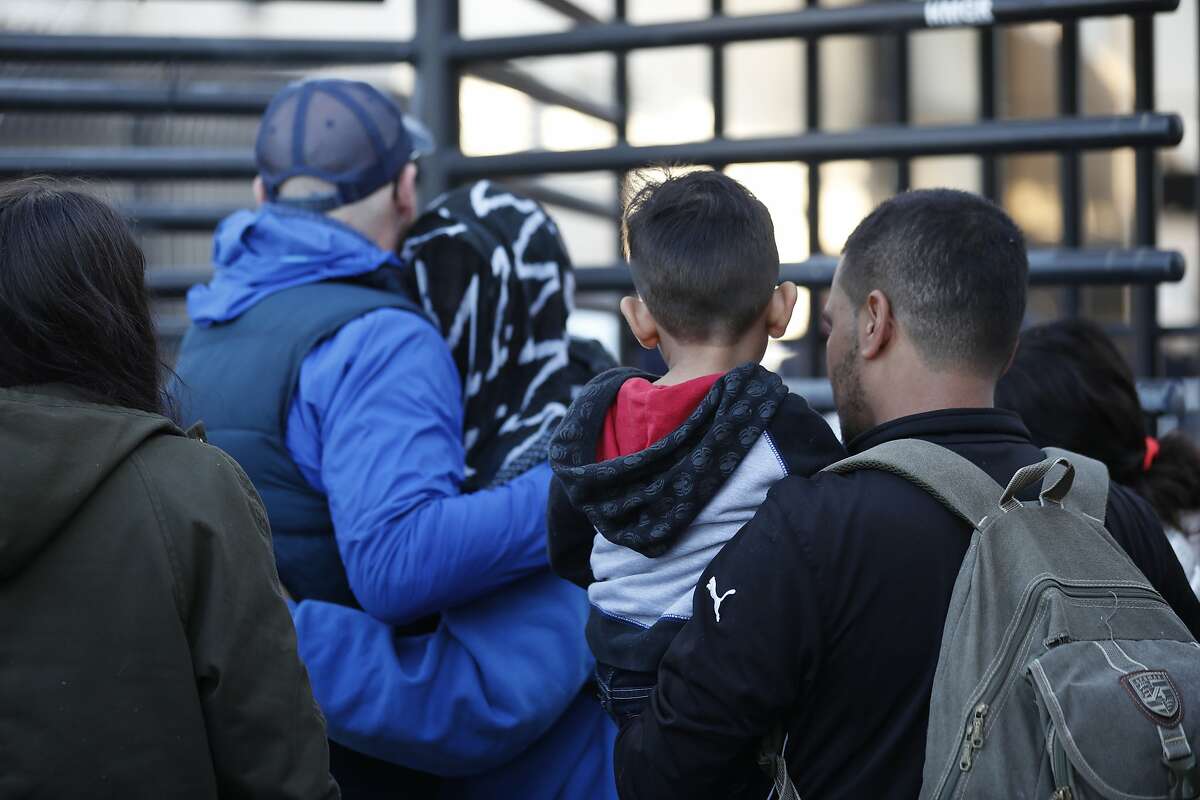 In this Dec. 18, 2018 photo, Honduran asylum seekers enter the U.S. at San Diego's Otay Mesa port of entry, as seen from Tijuana, Mexico. A federal judge has blocked restrictive Trump administration policies that prevented some immigrants from seeking asylum due to domestic and gang violence in their home countries. (AP Photo/Moises Castillo)