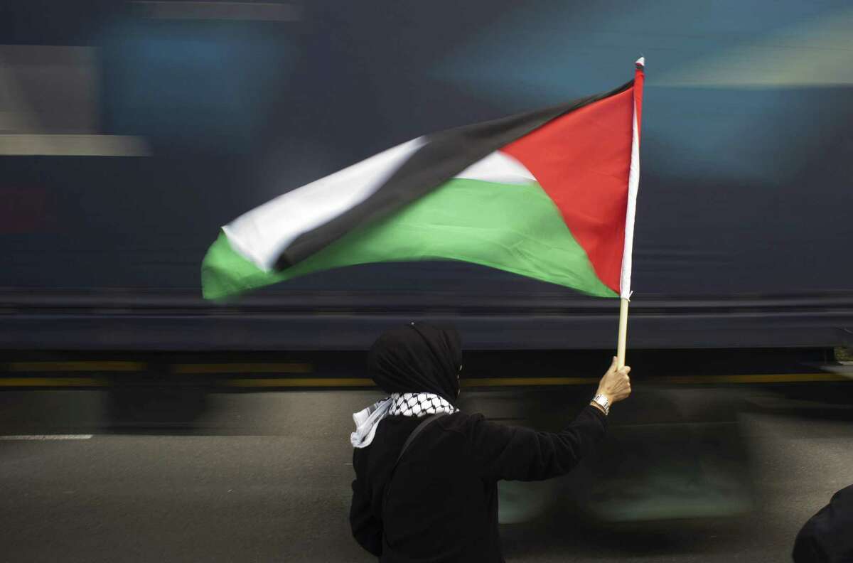 TOPSHOTS A woman holds a Palestinian flag as a truck passes by, during a protest against Grammy-winning American musician Pharrell Williams near the Grand west Casino where he was holding a concert in Cape Town, on 21 September, 2015. Supporters of the Boycott, Divestment and Sanctions (BDS) campaign were protesting against the singer's partnership with major South African retail group Woolworths, over its imports from Israel. BDS accuses Woolworths of importing Israeli agricultural produce grown in the occupied Palestinian territories, a charge the company denies. AFP PHOTO / RODGER BOSCHRODGER BOSCH/AFP/Getty Images