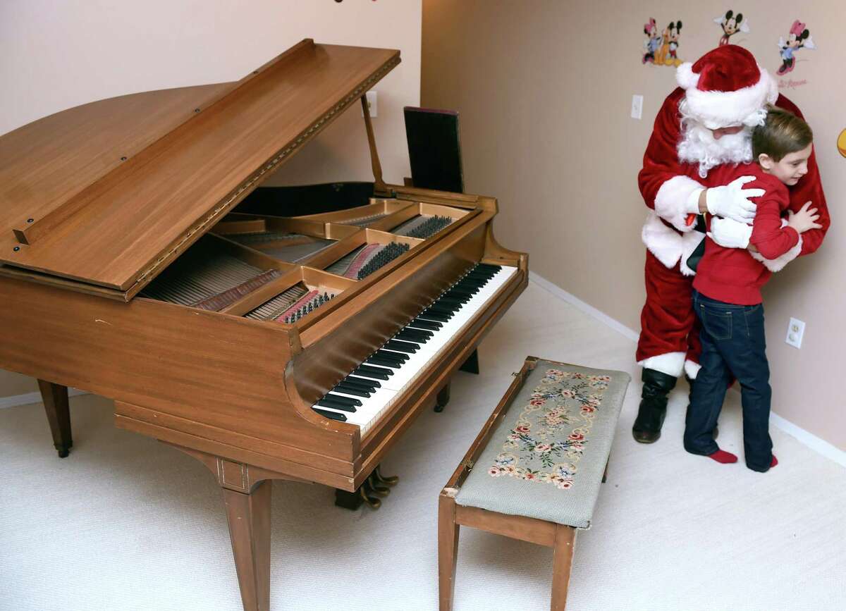 Alexander Stamboulidis, 9, thanks Santa Claus for the delivery of his Christmas wish, a baby grand piano, to his home in North Haven on December 24, 2018. Michael Storz, president of the Chapel Haven Schleifer Center, filled in for Santa Claus.