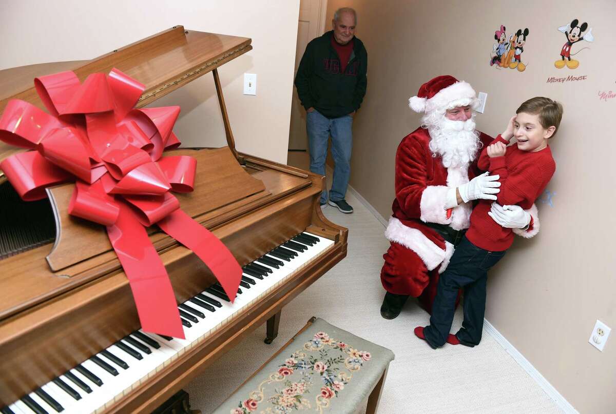 Alexander Stamboulidis, 9, thanks Santa Claus for the delivery of his Christmas wish, a baby grand piano, to his home in North Haven on Christmas Eve. Michael Storz, president of the Chapel Haven Schleifer Center, filled in for Santa Claus.