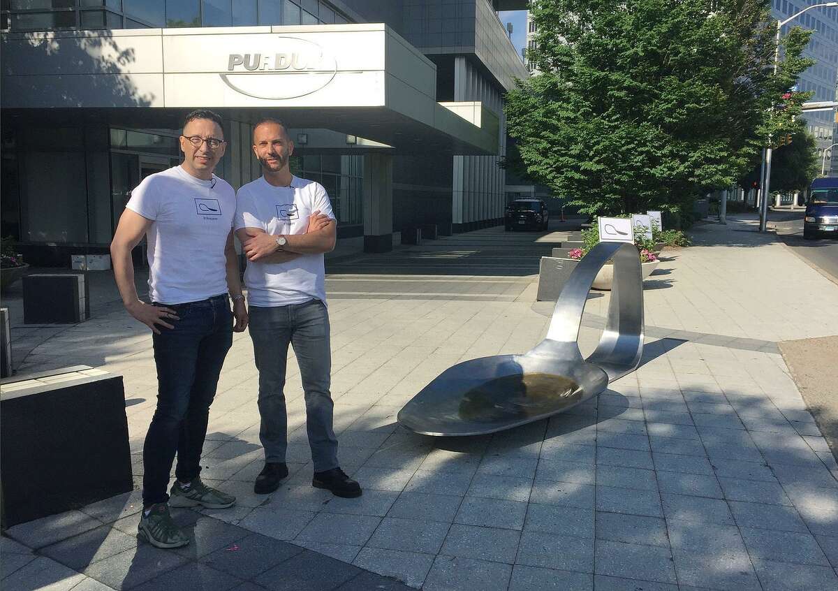 Art gallery owner Luis Alvarez, left, and sculptor Domenic Esposito stand with an 800-pound sculpture of a bent, burnt heroin spoon placed in front of the Purdue Pharma headquarters in June. Alvarez plans to close his downtown Stamford gallery in January.