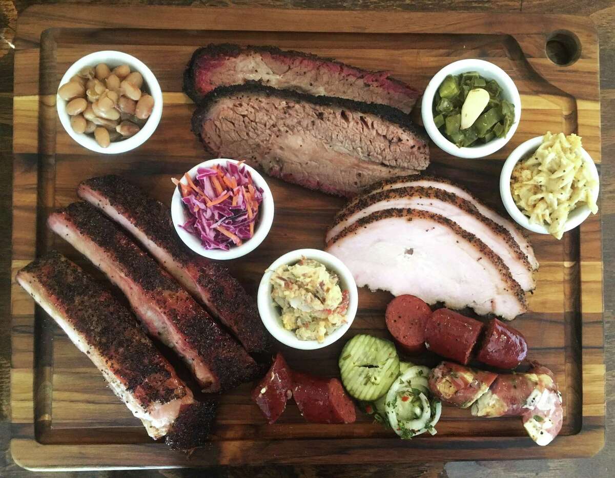 San Antonio’s 2M Smokehouse board (from top left) includes: borracho beans, brisket, nopales, chicharoni macaroni, turkey, beef sausage link, pork serrano and Oaxacan link, house-made pickles and onions, potato salad, pork ribs and coleslaw.