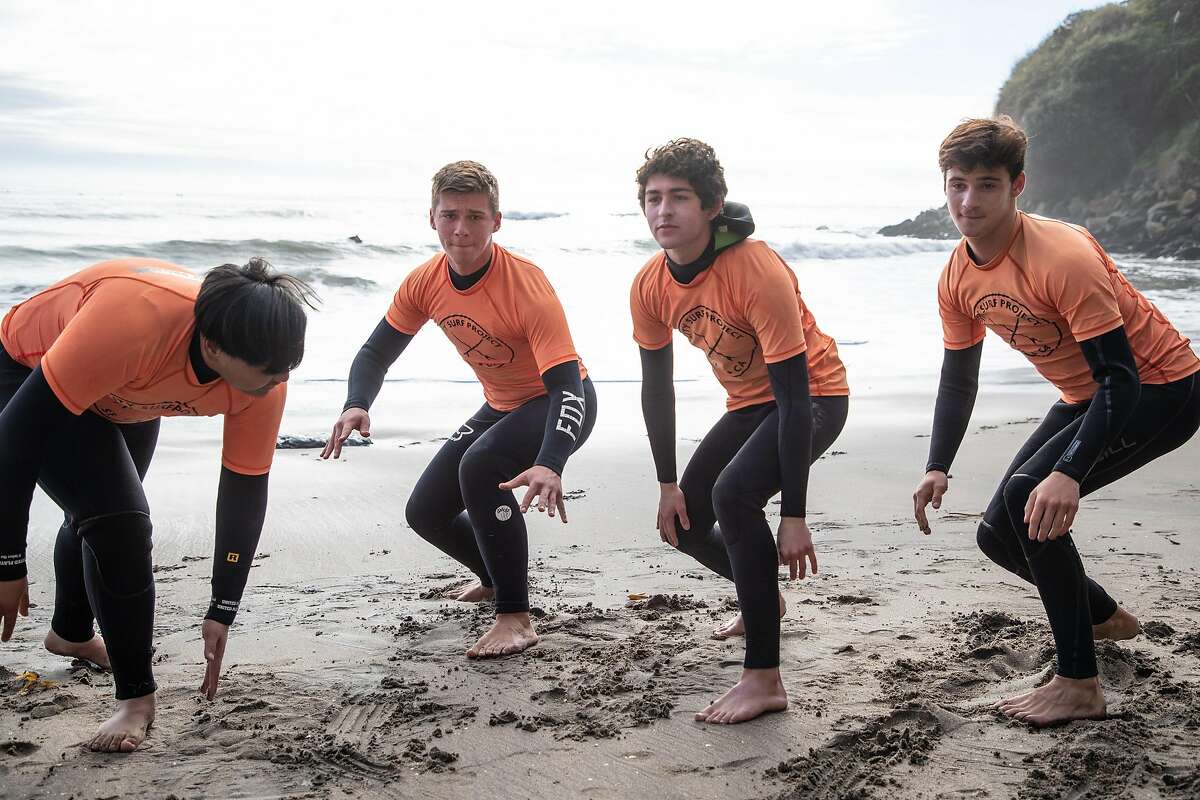Students Ian Zapanta, 14, at left, Sam Catechi, 15, Matan Maoz, 17, and Lucian Scher, 16, practice the motions of getting up on a surf board at Private's Beach as City Surf Project takes a group of Mission High School students surfing on Friday, Dec. 21, 2018, in Santa Cruz, Calif.