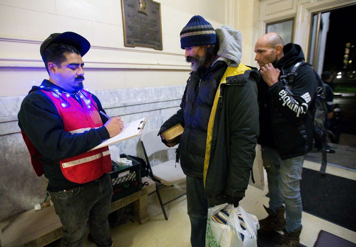 Berkeley, CA: On Christmas Eve, shelter monitor Scott Moreno, 33 of Berkeley, checks in Robert and Travis Blea to the Berkeley Emergency Storm Shelter which operates out of Old City Hall on rainy days as well as when temperatures drop below 40 degrees Fahrenheit. December 24, 2018. Photo by Lisa Hornak