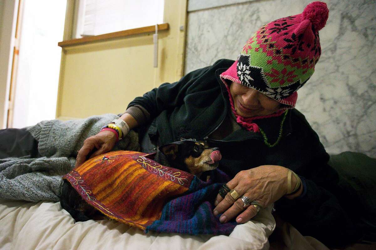 Berkeley, CA: On Christmas Eve, Elizabeth Bolanco, 68, settles in for the night with her dog Houdini at the Berkeley Emergency Storm Shelter to open. It operates out of Old City Hall on rainy days as well as when temperatures drop below 40 degrees Fahrenheit. December 24, 2018. Photo by Lisa Hornak