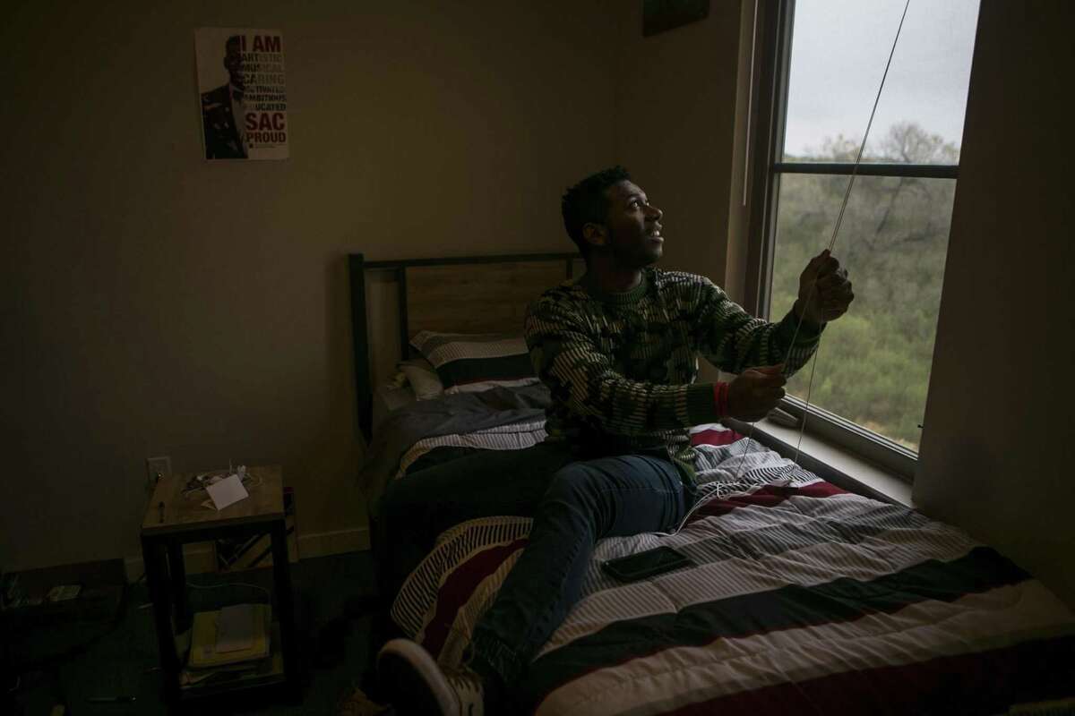 Miguel Alcorn, 22, pulls up his blind to the view of trees and brush from his dorm room in Esperanza Hall on the campus of Texas A&M University San Antonio.