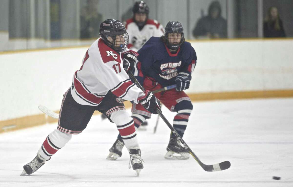 New Canaan’s Justin Weitfeldt (17) passes the puck in front of NFI’s Mason Perragine on Thursday at the Danbury Ice Arena.