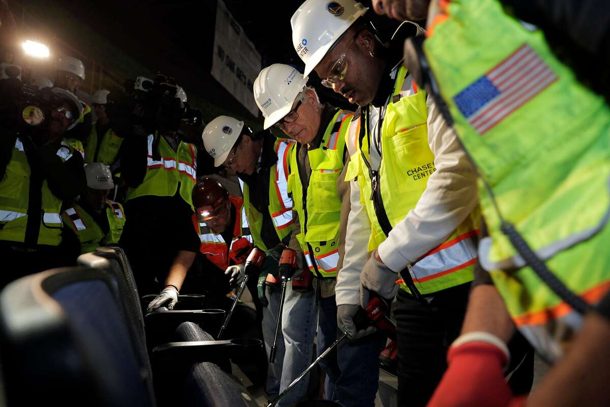 Season ticket holder Tim Leahy, center, was surprised with the opportunity to install his new seats with an assist by Warriors legend Tim Hardaway, at the new Chase Arena which is still under construction in San Francisco on Friday, Jan. 4, 2019. The seats were the first installed at the arena, and the Warrior will open their 2019-2020 season in the new facility.