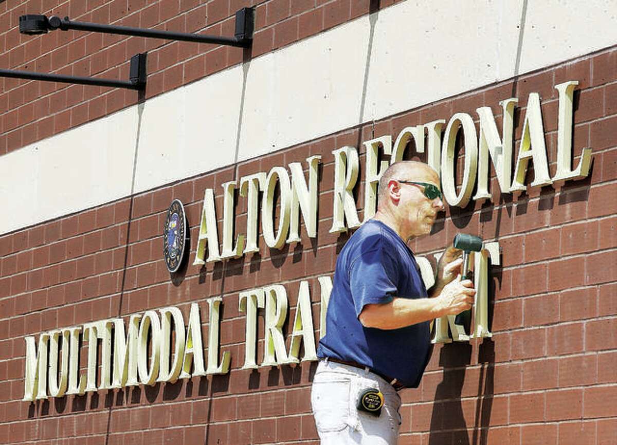 An employee of R.W. Boeker Co., Inc., in Hamel, uses a rubber mallet to tap a T into place for the lettering of the sign on the Alton Regional Multimodal Transportation Center.