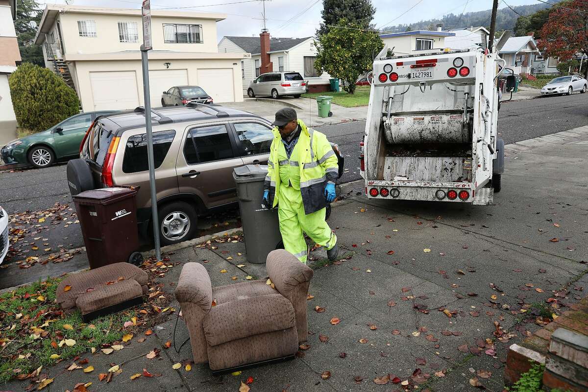 Ayinde Osayaba, Keep Oakland Clean and Beautiful public maintenance worker, prepares to pick up a chair to place it into the garbage truck as he and David Conti (not shown), Keep Oakland Clean and Beautiful public maintenance worker, work on Monday, December 17, 2018 in Oakland, Calif.