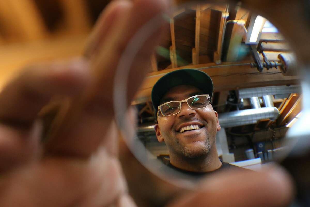 Jerry Harmon stands for a portrait behind a puck, a piece of glass for cutting a lens, while wearing a pair of eyeglasses he made at Topology on Monday, January 7, 2019 in San Francisco, Calif.